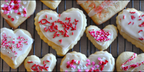 Heart-shaped cookies with white icing and red and pink sprinkles on a cooling rack.