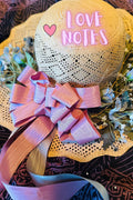 Decorative hat with 'LOVE NOTES' text and pink bow on a patterned background